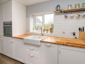 A modern kitchen with white cabinets, a wooden countertop, a built-in oven, a window with a view, and a shelf with jars and mugs. - Cysgod Y Coed (Machynlleth)
