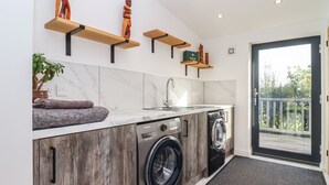 Une cuisine moderne dotée d’un lave-linge et d’un sèche-linge intégrés, de meubles en bois, de plans de travail en marbre et d’un paillasson noir à l’entrée.