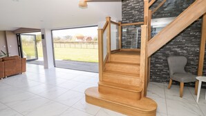 Un intérieur moderne avec un escalier en bois menant à un balcon, un fauteuil recouvert d’un tissu gris et un banc en bois.