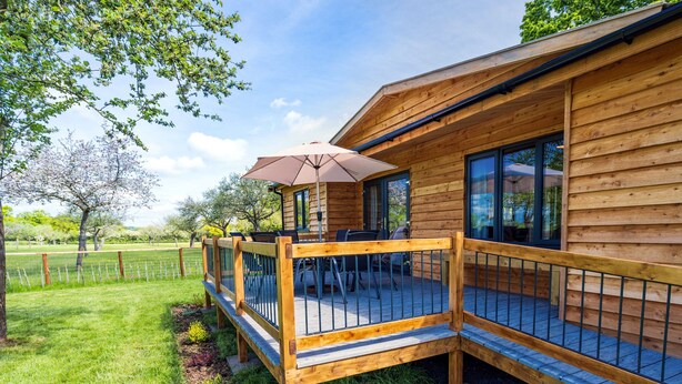 A wooden cabin with a deck, outdoor seating, and a large window.