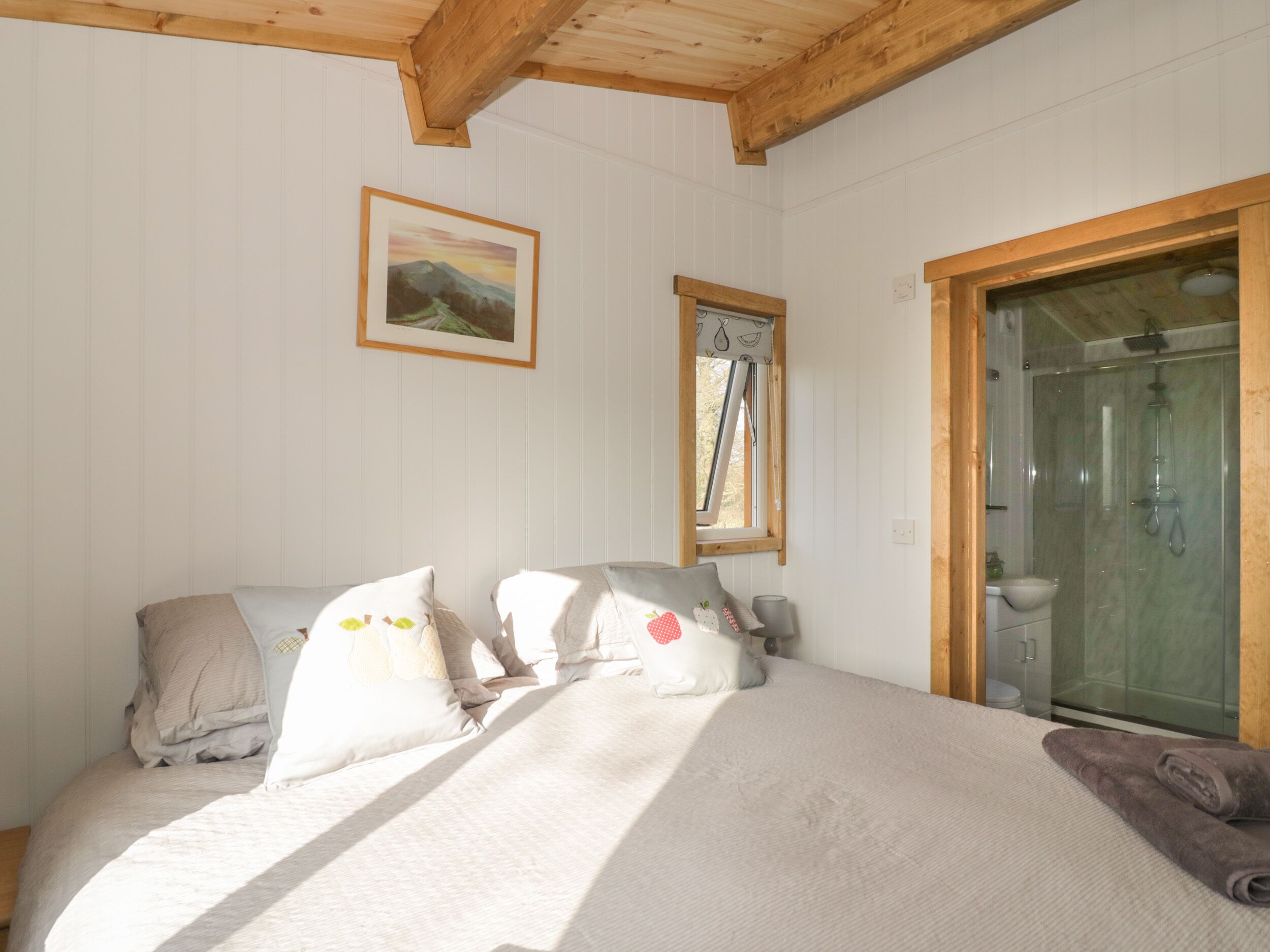 A bedroom with a bed, pillows, a framed picture, a window, and a shower area.