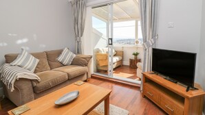 Ein Wohnzimmer mit Sofa, Couchtisch, TV-Schrank und einer Glastür, die zu einem Außenbereich führt.