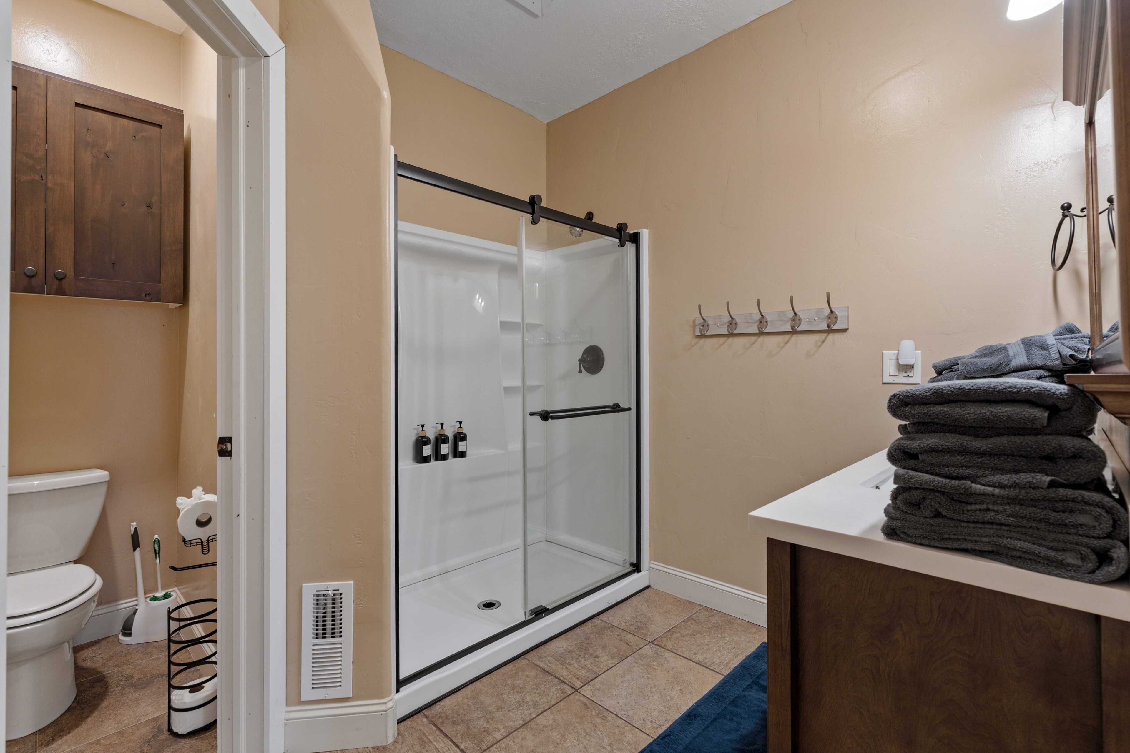 A bathroom with a glass shower enclosure, a toilet, a sink with towels, and a cabinet.
