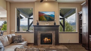 Una sala de estar con chimenea, un televisor grande montado encima y una vista panorámica a través de las ventanas.