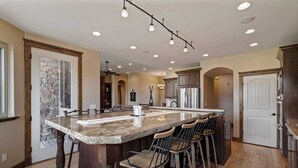 Una cocina con una isla grande, taburetes de bar, armarios de madera y un salpicadero de piedra.