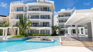 Un hotel de varios pisos con piscina, mobiliario exterior y palmeras.
