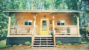 A wooden cabin with a front porch, a yellow door, and a small set of stairs leading to the entrance. - Cozy year round cabin in the woods, walking distance to the lake (Buck Lake AB)