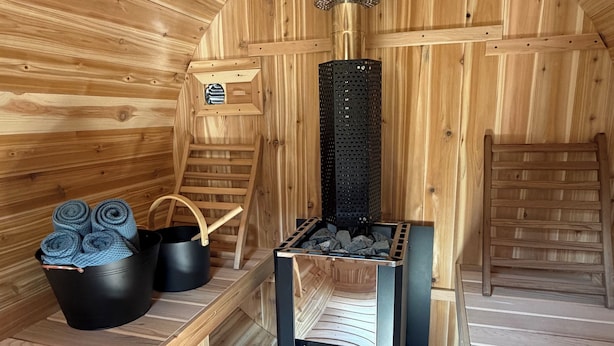 A sauna room with wooden walls, a sauna bench, a black heater, and a wooden ladder. - Cozy year round cabin in the woods, walking distance to the lake (Buck Lake AB)