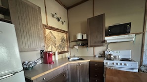 A compact kitchen with a refrigerator, a microwave, a stove, and a coffee maker. - Cozy year round cabin in the woods, walking distance to the lake (Buck Lake AB)