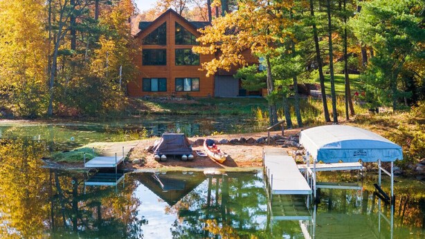 A cabin with a dock extending into a calm lake, surrounded by autumn foliage.
