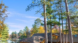 A cabin with a deck, surrounded by tall trees and a body of water.