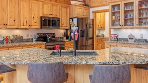 A kitchen with wooden cabinets, granite countertops, stainless steel appliances, and a bar area with bar stools.