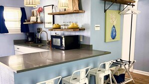A modern kitchen with a central island, bar stools, a coffee machine, and hanging lights.