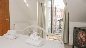 A bedroom with a bed, a dresser, and a view of buildings through a window. - Beach House (Colwyn Bay)