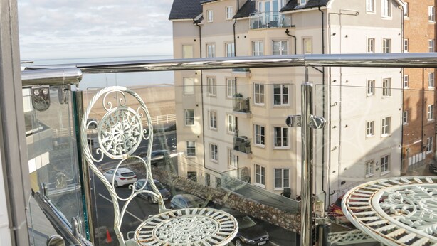 A balcony with ornate metal railings and a clear view of multi-story buildings in the background. - Beach House (Colwyn Bay)