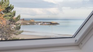 A coastal view from a window, including a sandy beach, calm sea, and a few boats. - Beach House (Colwyn Bay)