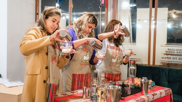 Tres personas preparando bebidas en un bar con varias botellas y vasos.