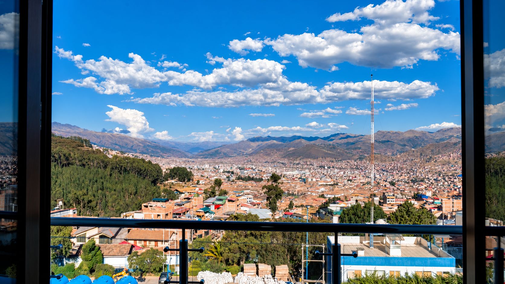 Une vue panoramique d’une ville, avec des montagnes en arrière-plan, un ciel dégagé et une tour imposante.