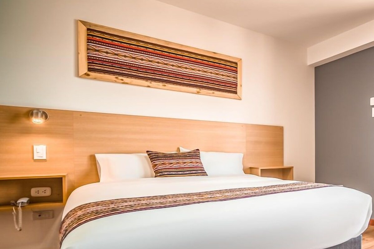 A modern hotel room with a large bed, wooden headboard, and a decorative wall piece.