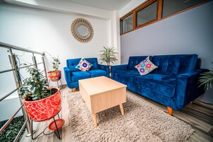A modern living room with a blue sofa, a wooden coffee table, and a red potted plant.