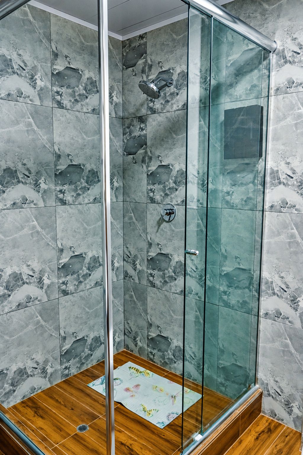 A glass-enclosed shower with marble walls and a wooden floor.