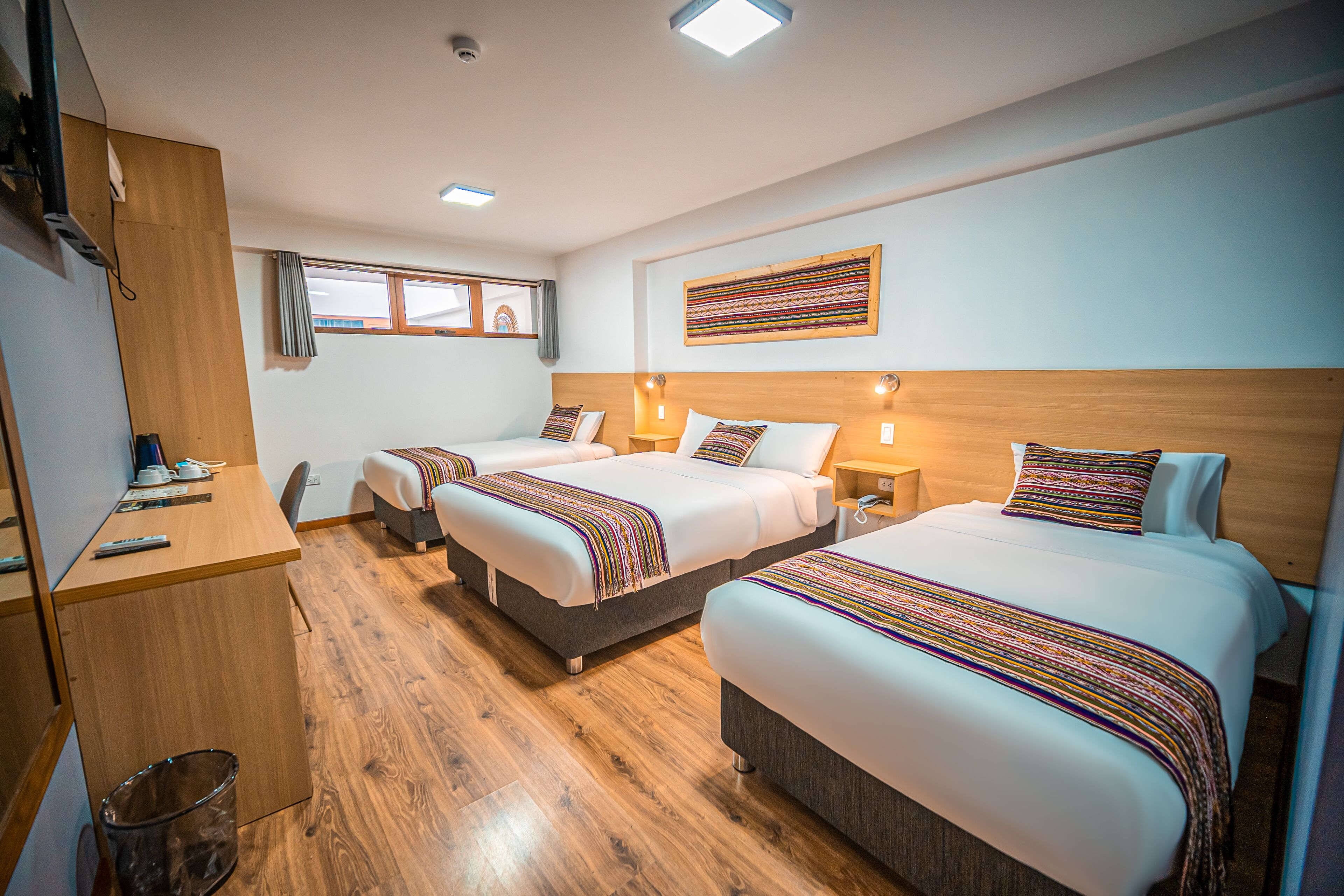 A hotel room with two beds, a wooden desk, a trash bin, and a window.
