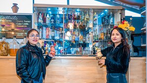 Zona de bar con una variedad de botellas de licor y un panel con la lista de cócteles.