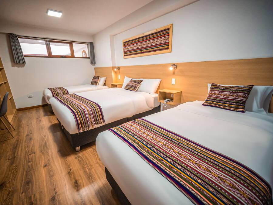 A hotel room with two beds, wooden flooring, and a window with curtains.