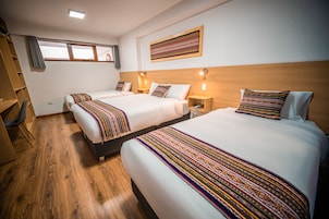 A hotel room with two beds, wooden flooring, and a window with curtains.