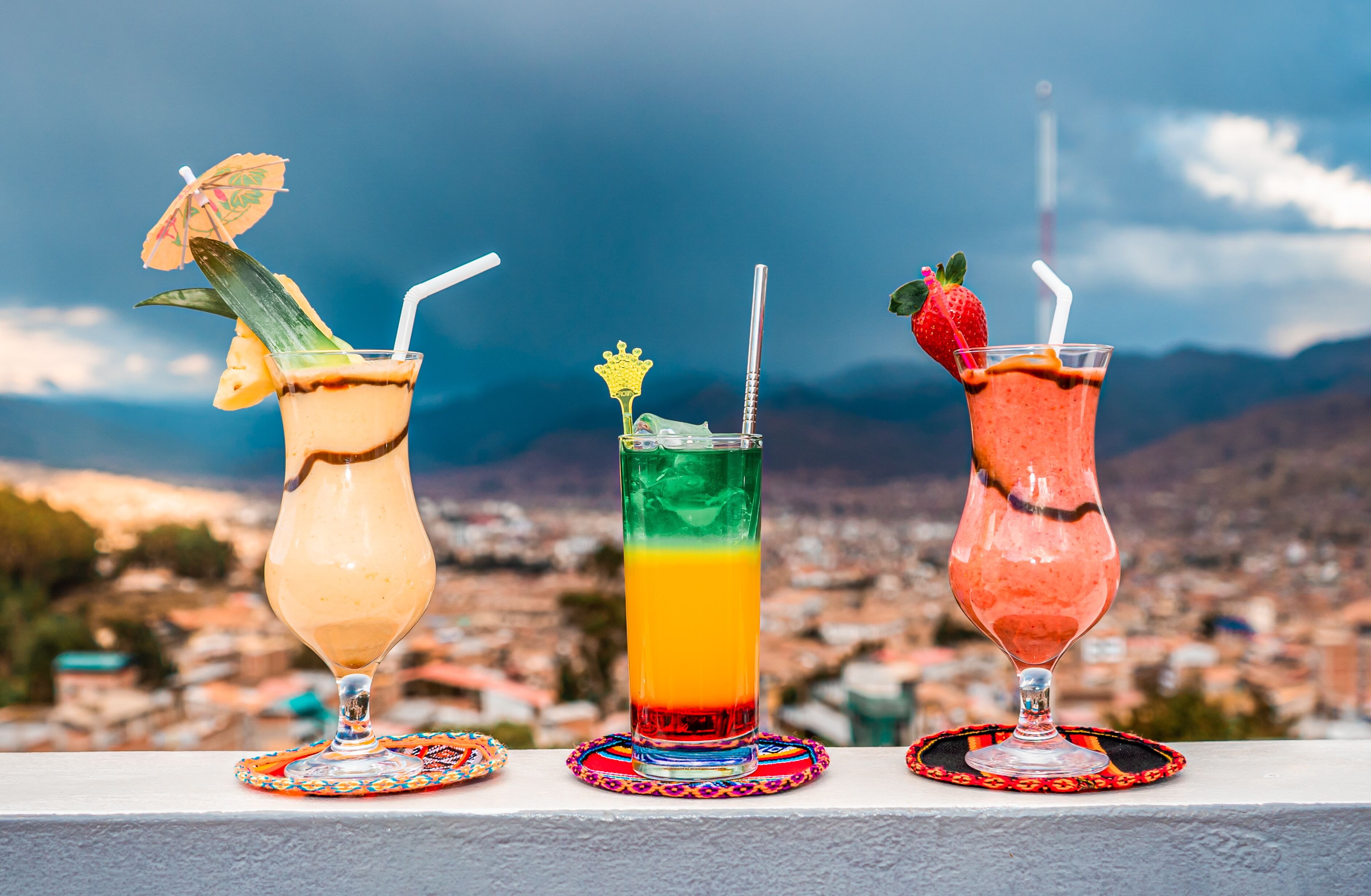 Three cocktails on a balcony with a cityscape view.