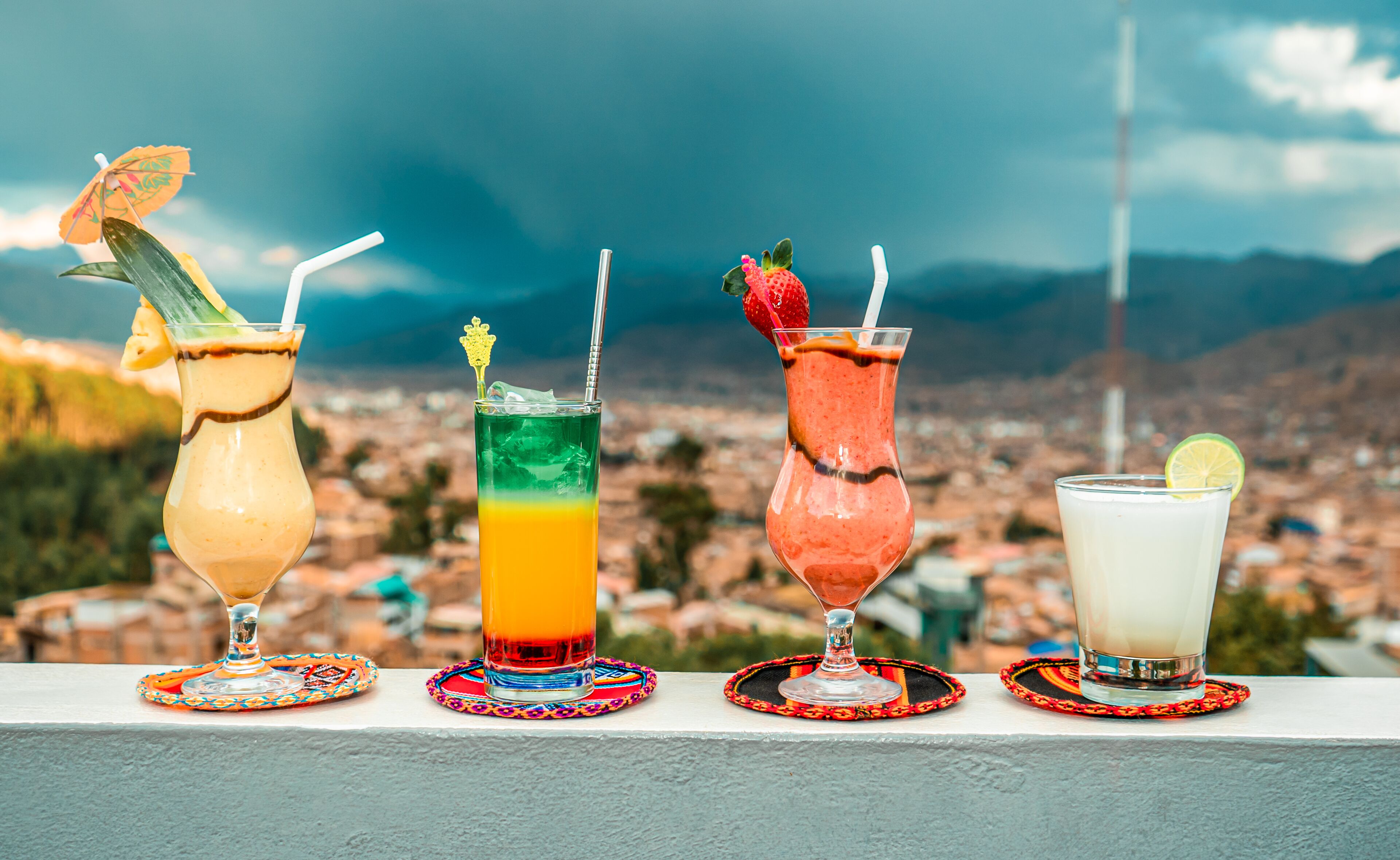 Four cocktails on a balcony with a cityscape view.