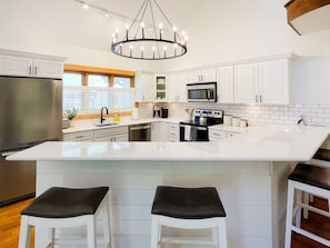A modern kitchen with white cabinetry, a large island with stools, stainless steel appliances, and a chandelier.