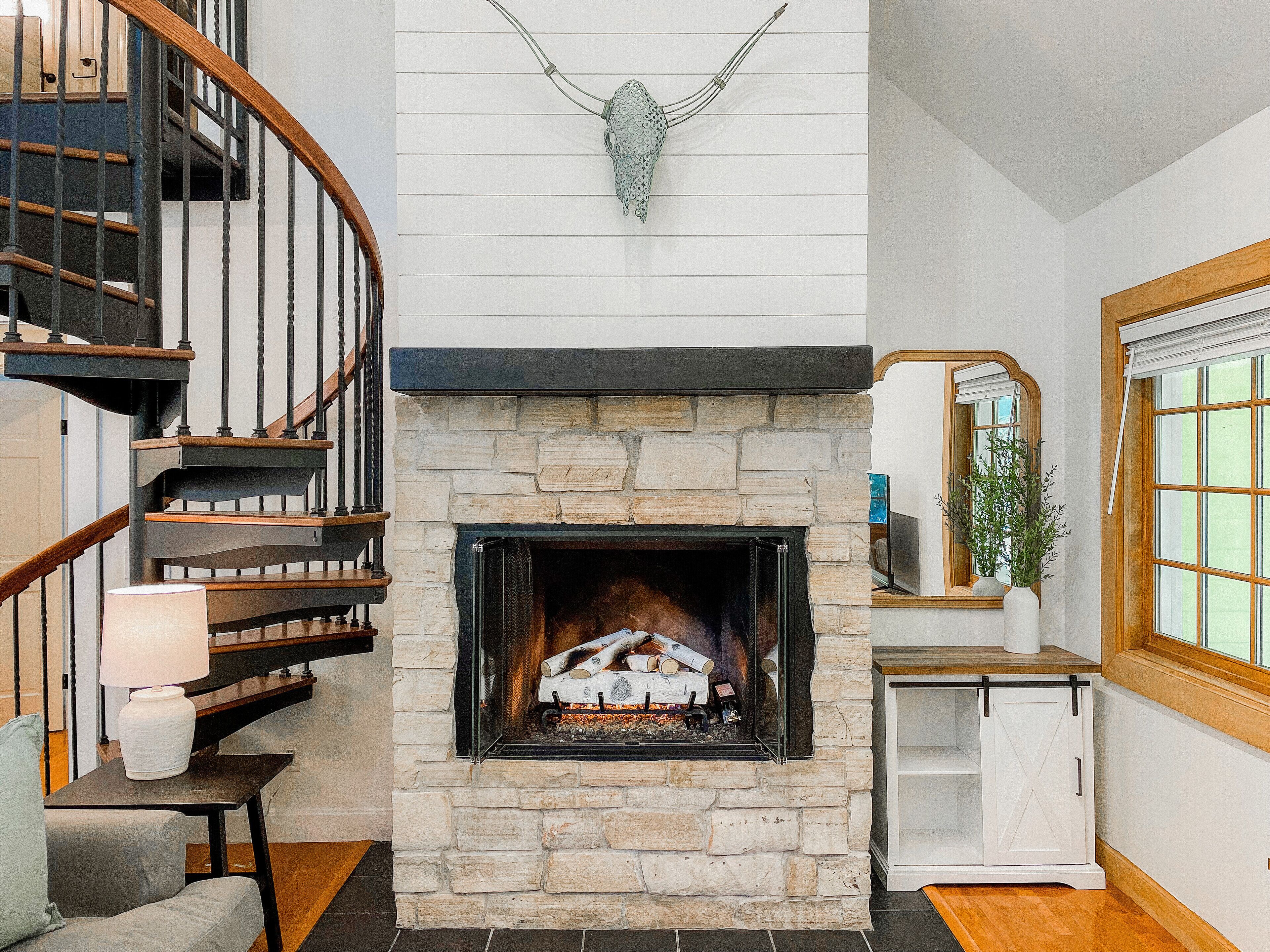 Une cheminée en pierre avec un feu de bois, un escalier en bois et une armoire blanche.
