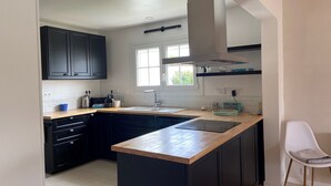 A modern kitchen with dark cabinets, a wooden countertop, a built-in sink, and a window providing natural light. - House sleeps 8 near Luzeronde (Noirmoutier-en-l'Île)