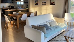 A modern living room with a white sofa, a dining area, and a kitchen in the background. - House sleeps 8 near Luzeronde (Noirmoutier-en-l'Île)