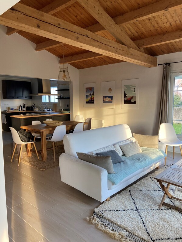 A modern living room with a white sofa, a dining area, and a kitchen in the background.