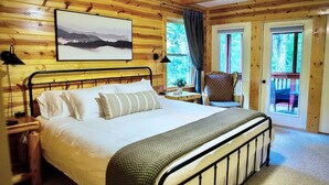 Camera da letto in una baita di legno, con un letto, un comodino, una sedia e una finestra con tende.