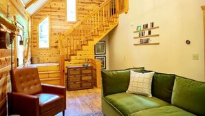 Accogliente interno di una baita in legno con una scala in legno, un divano verde e un settimino.