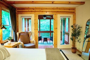 Habitación acogedora con cama, una silla, una mesa y una planta en maceta. Hay una ventana con cortinas y vistas al exterior.