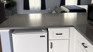 Eine moderne Küche mit weißen Schränken, einer Granit-Arbeitsplatte und einem integrierten Kühlschrank. Über der Kochinsel hängen zwei Pendelleuchten, und an der Decke befindet sich ein Deckenventilator mit Licht.