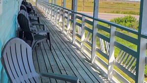 Eine überdachte Veranda mit Adirondack-Stühlen und Blick auf eine Straße und Felder.