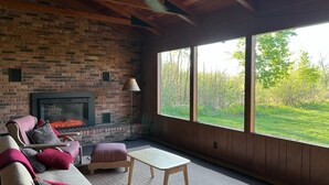 A cozy room with a brick fireplace, a large window, and a comfortable seating area. - Lake Cabin (Brainerd)