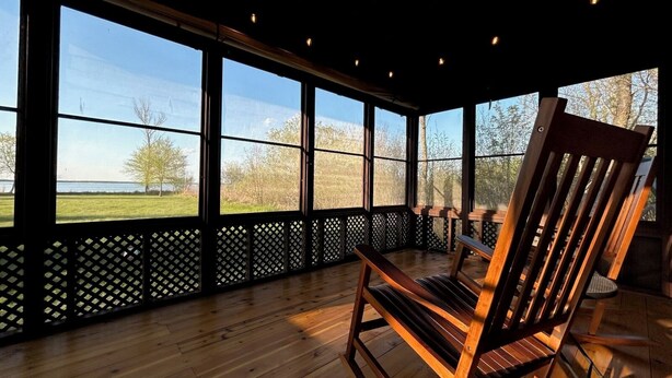A wooden rocking chair in a room with large windows overlooking a grassy area. - Lake Cabin (Brainerd)
