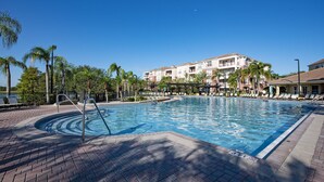 Ein Swimmingpool mit Backstein-Terrasse, umgeben von Palmen und einem Gebäude mit Balkonen.