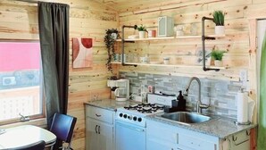 A compact kitchen with wooden walls, a gas stove, a sink, and a dining area with a table and chairs. - Modern lakeside cabin with panoramic views and deck. (Alexandria)