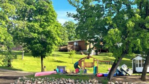 A playground with a slide, swings, and a wooden playhouse. - Modern lakeside cabin with panoramic views and deck. (Alexandria)