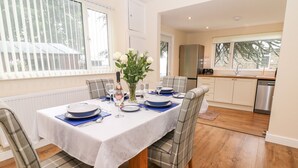 A dining area with a table set for four, a kitchen in the background, and a view of the outdoors through the window. - Cedar Holme (Chesterfield)