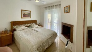 Ein Schlafzimmer mit Bett, Deckenventilator, Fernseher und einem Fenster mit Vorhängen.