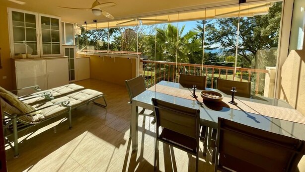 Ein Balkon mit Esstisch und Stühlen, einer Couch und einem Deckenventilator.