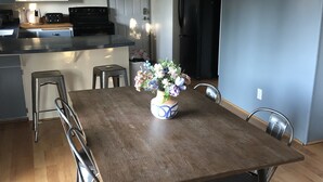 A dining area with a wooden table, metal chairs, and a vase of flowers. - Cozy home next to airport with fenced backyard and lots of sun! (Juneau)